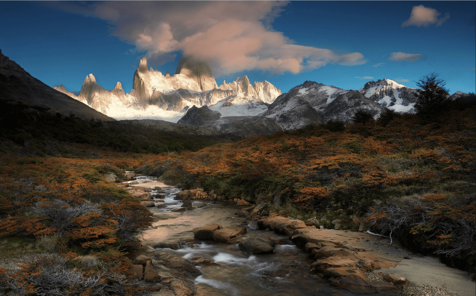 A creek running down the middle of a field with snow-capped mountains in the background